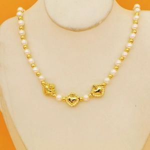 Collier de perles vintage avec pendentifs coeur dorés sur mannequin, fond orange