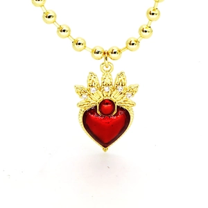 Détail d'une chaîne dorée à billes avec pendentif cœur rouge orné d'une couronne sertie