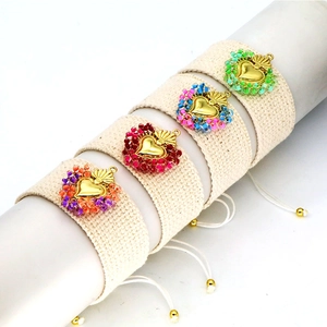 Detail view of four handmade woven bracelets featuring golden heart charms and seed beads
