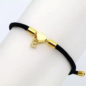 Detail of black woven rope bracelet with gold heart and pave zircon letter E charms