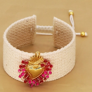 Close-up of handmade woven bracelet with golden sacred heart pendant and red beads