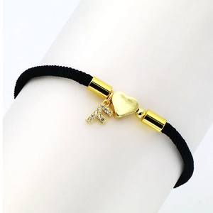 Detail of black woven cord bracelet with gold heart and zircon letter F pendant
