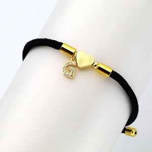 Detail of black braided cord bracelet with golden heart charm and zircon initial G pendant