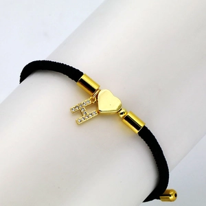 Detail of black woven bracelet with golden heart and zircon letter H on display