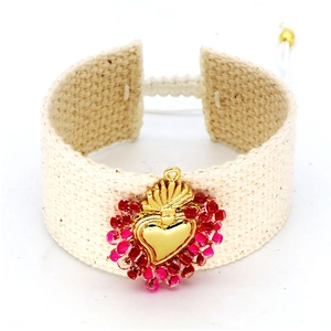 Detail of bohemian hand-woven cream cord bracelet with a gold heart and red beads