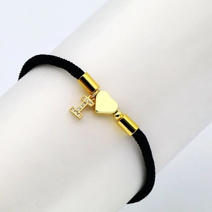 Detail of black cord bracelet with gold heart and letter I charm featuring zircons