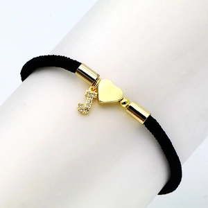 Detail of black woven bracelet featuring gold heart charm and micro-pave zircon letter J