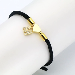 Detail of black woven rope bracelet with gold heart charm and zircon letter M pendant