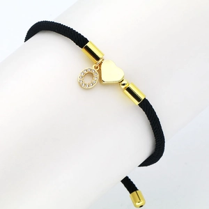 Detail view of a black braided bracelet with a golden heart charm and cubic zirconia ring