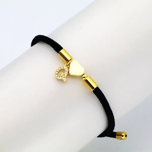 Close-up of black braided cord bracelet with gold heart charm and zircon letter Q