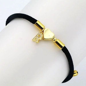 Detailed macro view of black cord bracelet with gold heart charm and zircon letter R