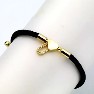 Detail of black braided rope bracelet with gold heart and zircon letter U charm