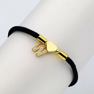 Macro detail of black braided bracelet featuring a gold letter W and heart charm