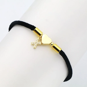 Detail of black woven rope bracelet with gold heart and zircon cross charms on a display