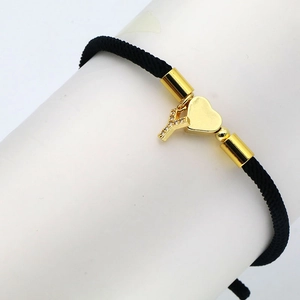 Detail of black braided cord bracelet with golden heart and zircon Y letter charms