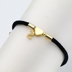 Detail of black woven cord bracelet featuring gold heart charm and Z letter in cubic zirconia