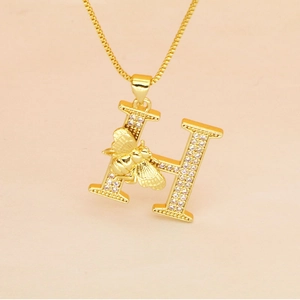 Macro detail of gold letter H pendant with micro-pave zircons and a small golden bee