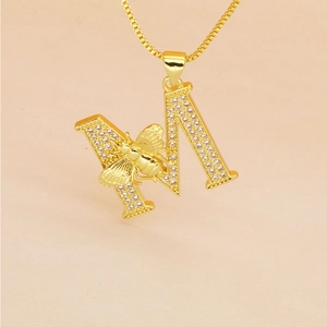 Close-up of golden letter M pendant with paved crystals and a 3D bee on a box chain