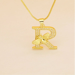 Macro shot of gold letter R pendant with micro-pave crystals and a small bee detail