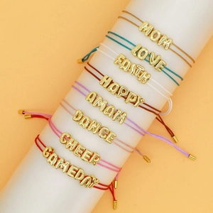 Detailoverzicht van kleurrijke gevlochten armbanden met gouden bedeltjes in lettervorm