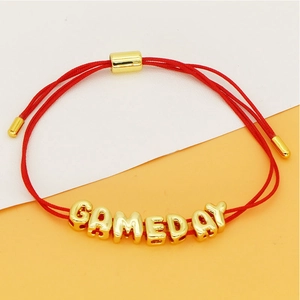 Detail van de rode geweven armband met gouden GAMEDAY-letterkralen en verstelbare sluiting