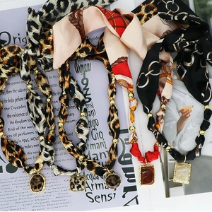 Dettaglio di collane foulard in seta con stampa leopardata, perline d'oro e pendenti