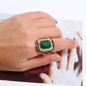 Vintage gold ring with emerald cut green stone and diamond halo on model hand