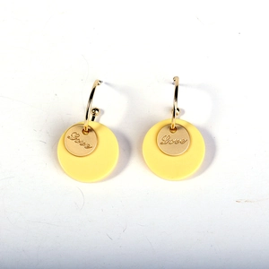 Detailed shot of yellow round earrings with golden hooks and small Love engraved discs