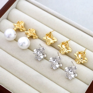 Irregular textured gold and silver earrings with white pearl accents on velvet tray