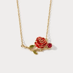 Macro detail of gold rose necklace with red enamel petals and emerald green leaf accents