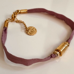 Pulsera de cinta rosa con cuenta de tubo dorada y cadena ajustable en fondo blanco