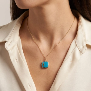 Vintage gold square locket necklace with turquoise enamel worn by a model on white shirt