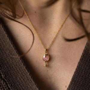 Gold wine glass pendant necklace with pink crystals on model neck in warm lighting
