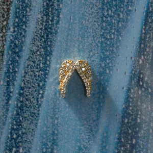 Colgante de alas de ángel dorado con brillantes diamantes blancos sobre fondo oscuro