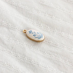 Oval botanical pendant with blue flower print on white ceramic and gold metal frame
