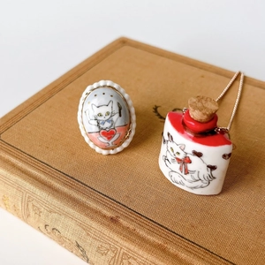 Close-up of cat pendant and necklace on vintage book showing detailed hand-painted ceramic