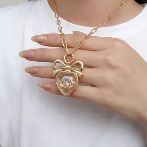 Détail d'un pendentif cœur doré avec nœud et breloques lune et étoiles sur une chaîne