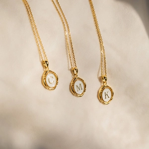 Détail des pendentifs lettres C, M et K dorés sur un fond en tissu plissé