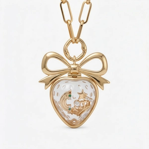 Détail macro du pendentif fraise avec nœud doré et petits charms rangés à l'intérieur