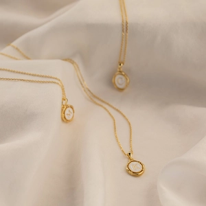 Détail de colliers dorés à pendentifs ovales avec lettres M, K, C sur du satin plissé