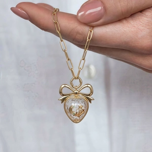 Détail d'un collier chaîne trombone en or avec un pendentif cœur transparent