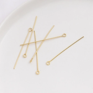 Detalle de alfileres de ojo dorados para bisutería DIY sobre un plato blanco