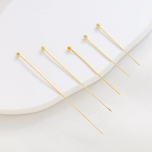 Five gold-plated ball head pins for DIY jewelry making on white textured background
