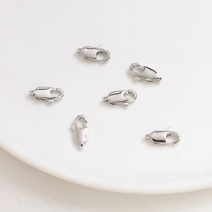 Close-up of six polished silver lobster clasps for DIY jewelry making on white ceramic