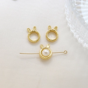 Detail of gold bunny ear charm spacers with white pearls on elegant silk background