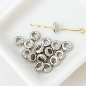 Macro shot of textured gold flower spacer beads and eye pin for DIY jewelry making