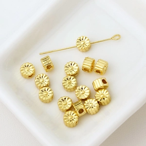 Macro shot of gold-plated flower spacer beads with textured petals in a white tray
