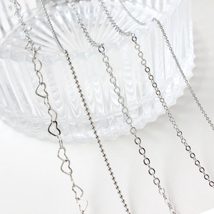 Assortiment de chaînes de bijoux argentées avec maillons cœur et ovales sur verre
