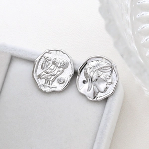 Macro detail of silver owl and Greek portrait pendant on white jewelry box tray