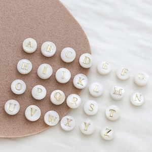 Macro shot of 8mm natural shell round beads with gold alphabet lettering for DIY jewelry